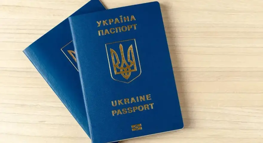 Dwa niebieskie paszporty biometryczne Ukrainy z złotym godłem i napisami leżą na drewnianym blacie.