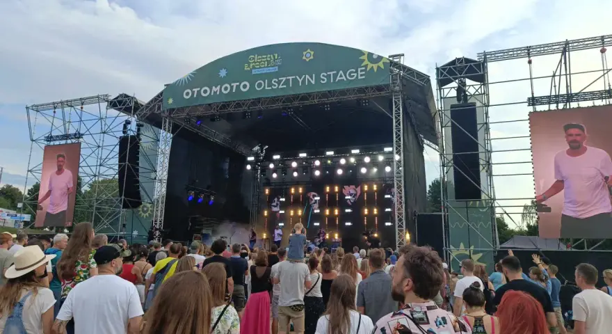 Tłum na festiwalu, na scenie OTOMOTO OLSZTYN STAGE. Kim Nowak w piasku, wśród ludzi.
