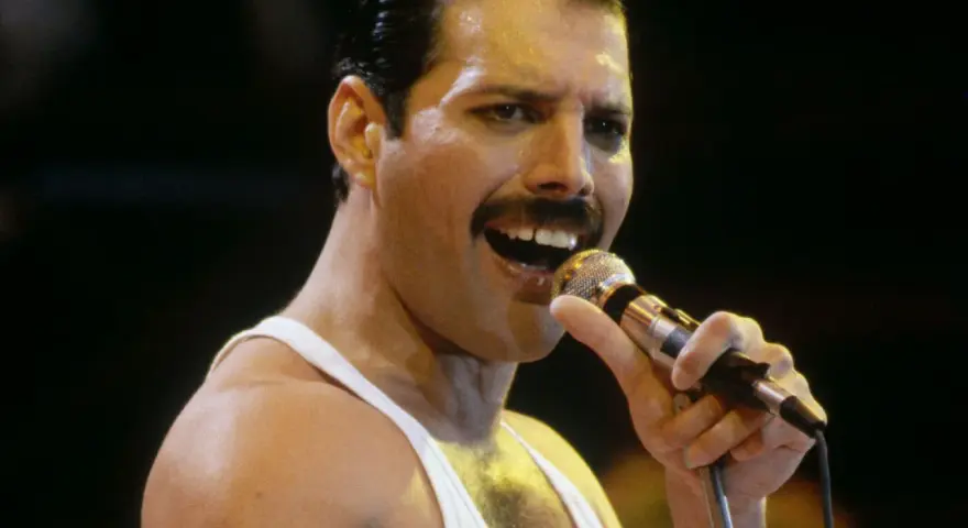 Freddie Mercury śpiewa do mikrofonu, w białej podkoszulce. Wiele osób wspomina go, kiedy zmarł Freddie Mercury.
