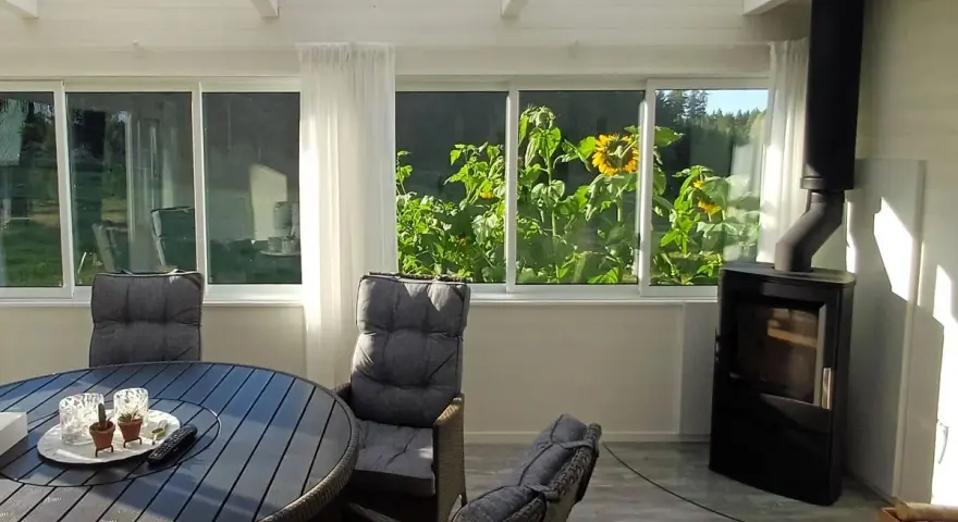 Mysig kamin i uterummet med solrosor utanför fönstret. Ett runt bord med stolar står redo för fika.