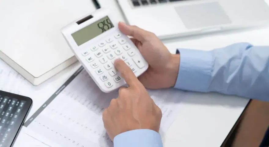 Persona calculando en calculadora blanca, revisando documentos y tablet. Se pregunta cuánto cuesta abrir una empresa en España.