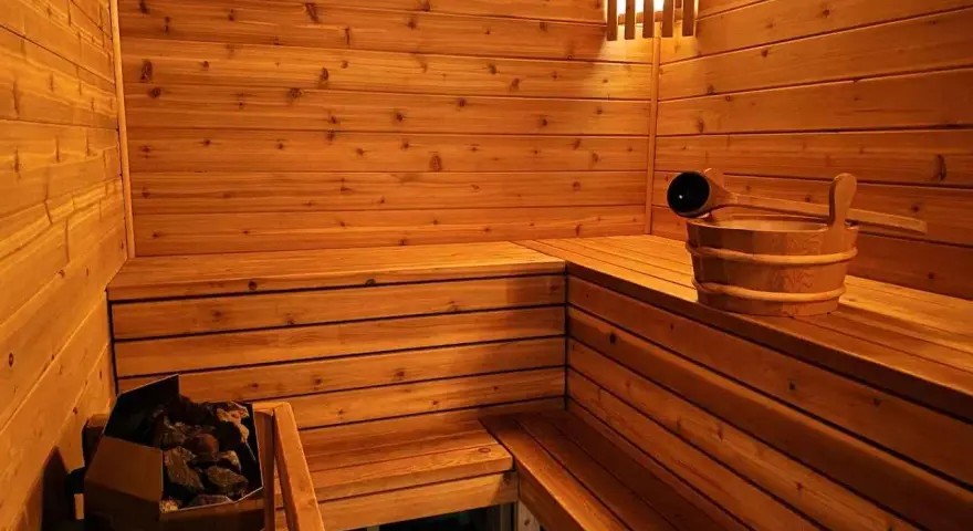 Drewniana sauna z kamieniami i wiadrem. Inspiracja, jak zbudować saunę, by cieszyć się relaksem.