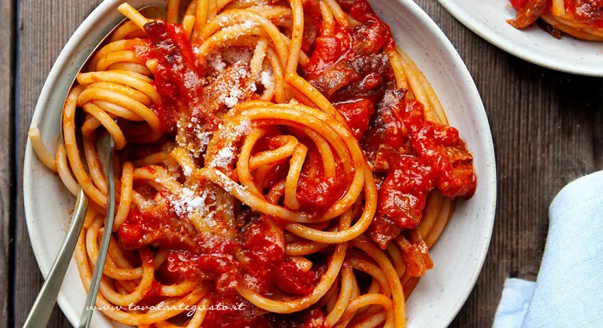 Un piatto fumante di spaghetti conditi con un ricco sugo all'amatriciana ricetta della nonna, cosparso di formaggio grattugiato.
