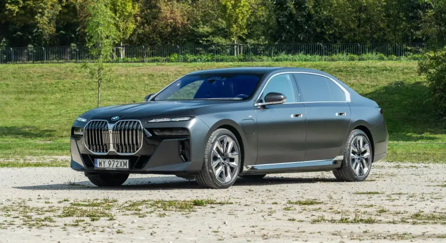 Elegancki, grafitowy BMW 740d na tle zieleni. Luksusowa limuzyna prezentuje się imponująco.