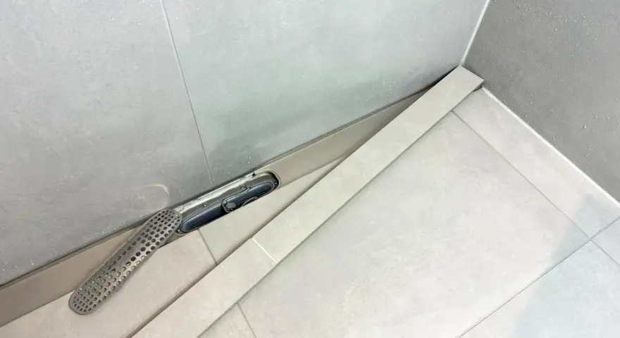 En dusch med en Purus vakuumventil och ett perforerat galler. Vatten droppar på de ljusa kakelplattorna.