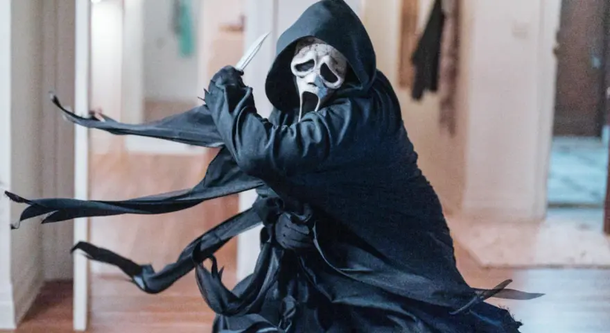 Ghostface, icona del film horror slasher, brandisce un coltello in un corridoio.