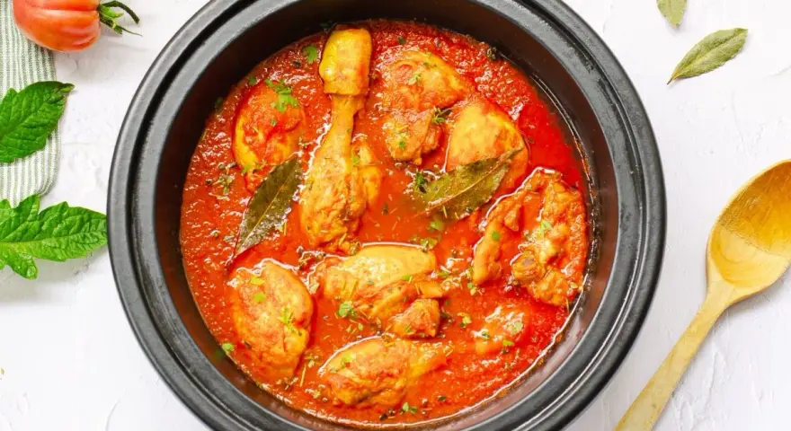 Pollo en salsa de tomate casera en olla negra, con hojas de laurel y perejil picado.
