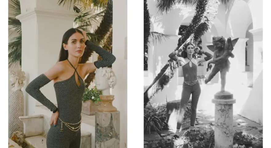 Modella con tuta scintillante e guanti lunghi, ispirata ai coco chanel abiti iconici, posa accanto a statue classiche in un giardino lussureggiante.