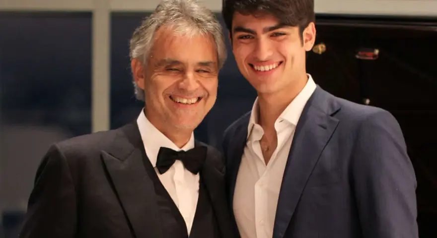 Andrea Bocelli młody i jego syn Matteo, obaj uśmiechnięci, w eleganckich strojach.