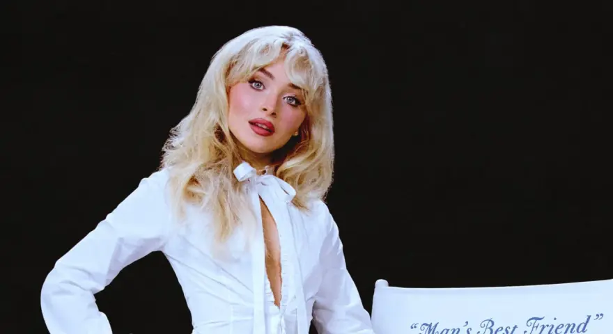 Sabrina Carpenter w białej koszuli, z rozpuszczonymi blond włosami, wygląda jak "man's best friend" na tle czerni.