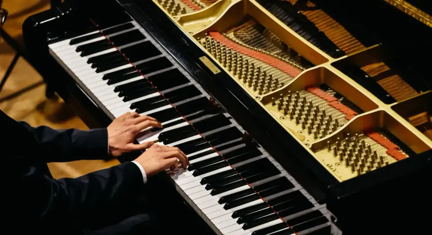 Dłonie muzyka grające na fortepianie, którego wnętrze z widocznymi strunami i młoteczkami przypomina zaawansowany piano vst.