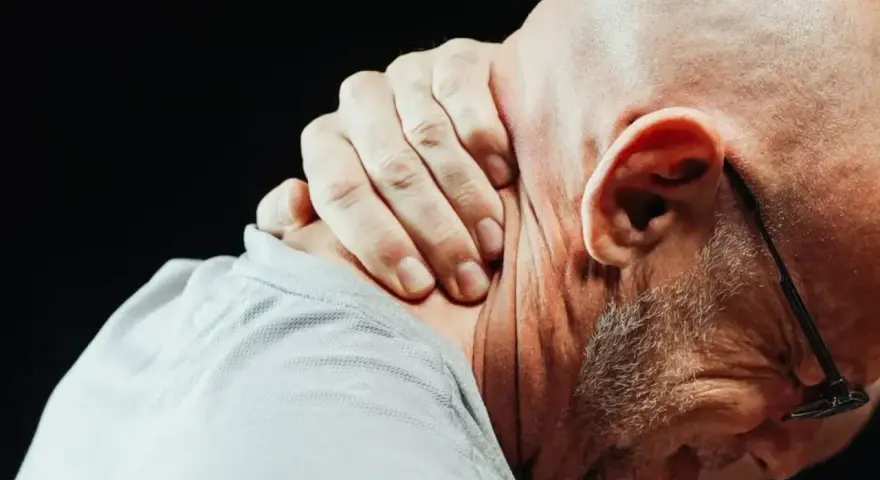 Mężczyzna trzyma się za kark, odczuwając ostry ból szyi przy skręcaniu głowy.