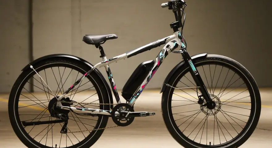 A white GT power performer electric bike with a colorful geometric pattern, parked indoors.