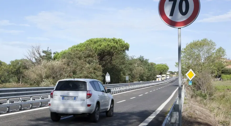Un'auto bianca percorre una strada extraurbana secondaria, superando un cartello di limite di velocità a 70 km/h.