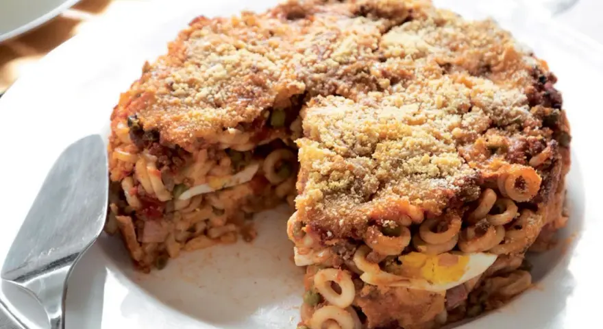 Un invitante anelletti al forno, con strati di pasta, sugo, piselli e uova sode, ricoperto da pangrattato dorato.