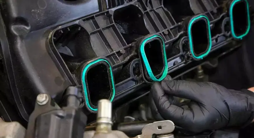 A gloved hand installs a new intake manifold gasket, ensuring a tight seal for optimal engine performance.