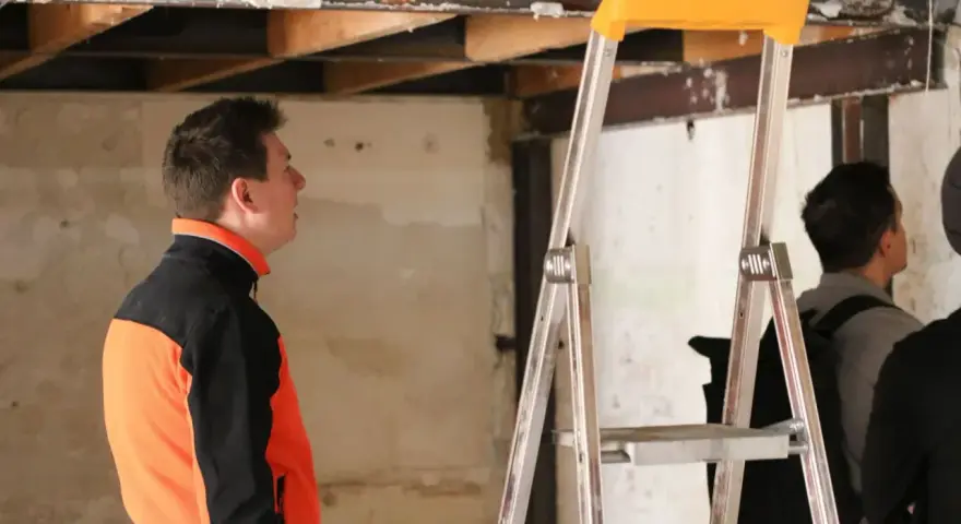 Un homme en veste orange et noire observe le plafond délabré d'un chantier. L'architecte assure le suivi de chantier, une obligation pour garantir la qualité des travaux.