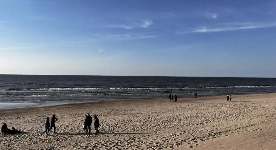 Plaża nad Bałtykiem z kilkoma spacerującymi osobami i widokiem na morze.