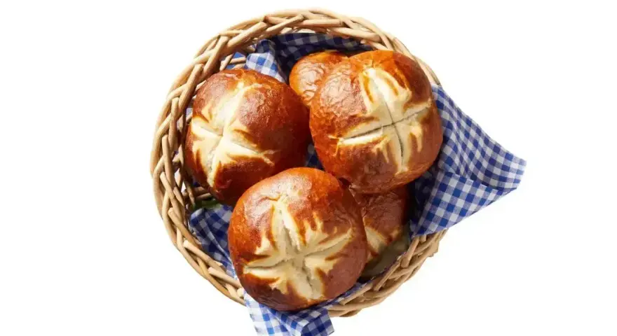 Koszyk z kilkoma bułkami bawarskimi, ułożonymi na niebiesko-białej kratkowanej serwetce.