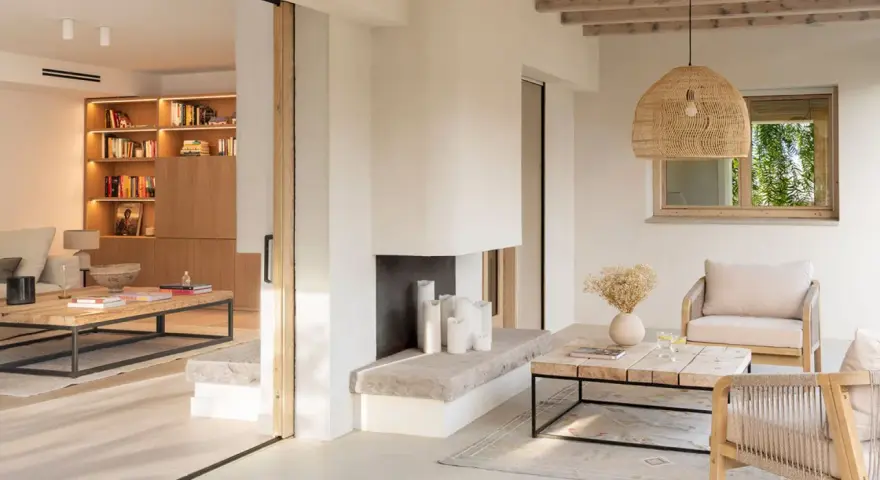 Salón luminoso con chimenea de piedra, muebles de madera y textiles naturales, evocando un relajante estilo ibicenco.