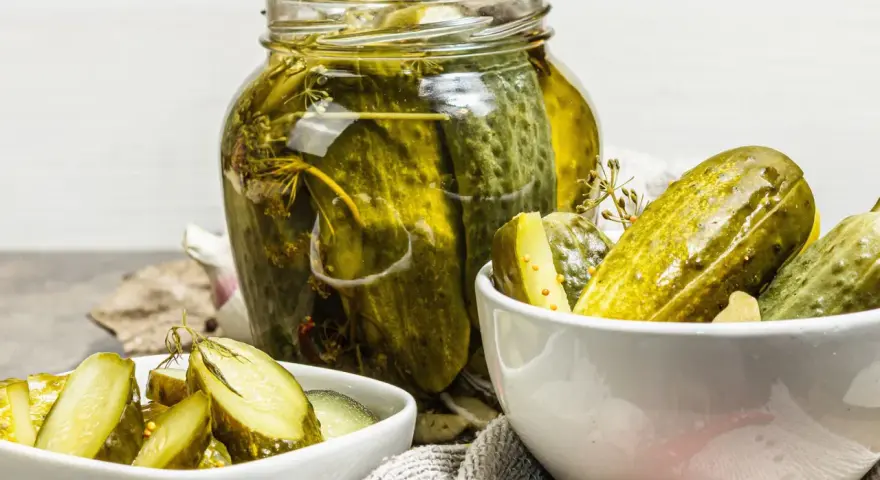 Cetrioli in agrodolce in un barattolo di vetro e in ciotole, con aglio e spezie.