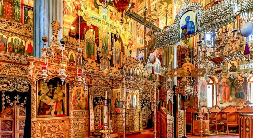 Interior of a richly decorated Orthodox church, showcasing ornate iconostasis, frescoes, and chandeliers, typical of many ancient christian monasteries.