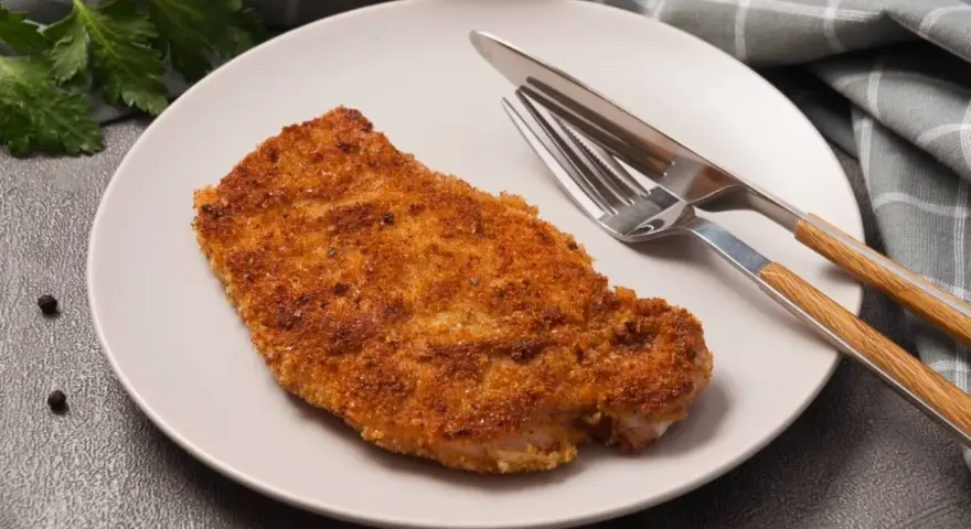 Kotlet schabowy w panierce na talerzu z widelcem i nożem.
