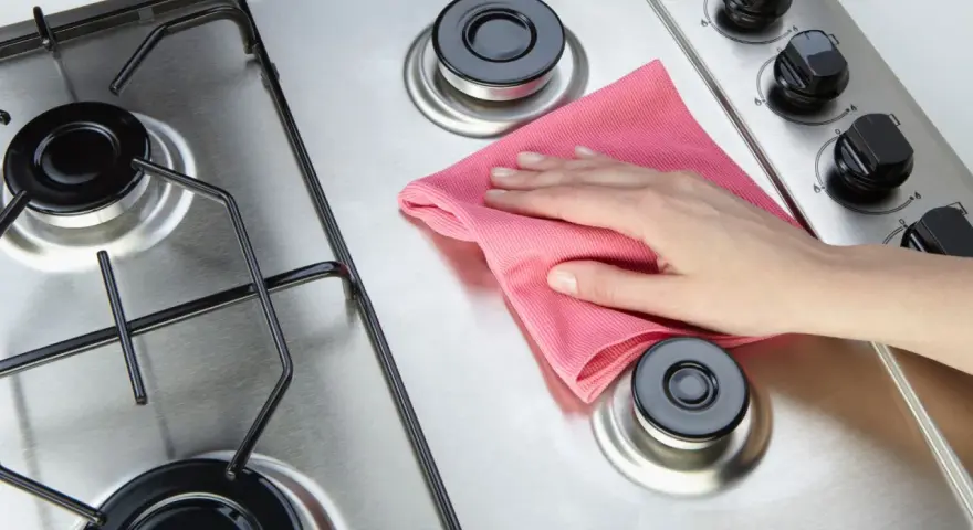 Mano con panno rosa lucida il piano cottura in acciaio.