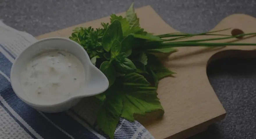Sauce tartare maison crémeuse dans un ramequin blanc, accompagnée d'herbes fraîches sur une planche en bois.