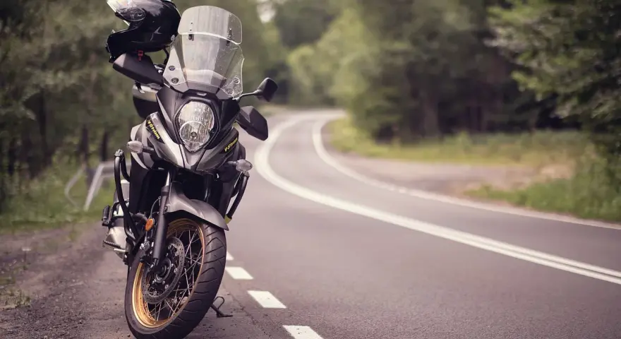 Moto pronta per avventurosi itinerari in moto su una strada tortuosa tra alberi. Casco appoggiato sul manubrio.