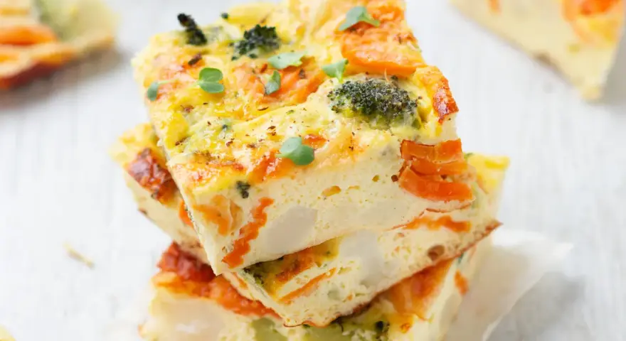 Fette di frittata al forno con verdure, broccoli e carote, guarnita con germogli freschi. Un piatto colorato e salutare.