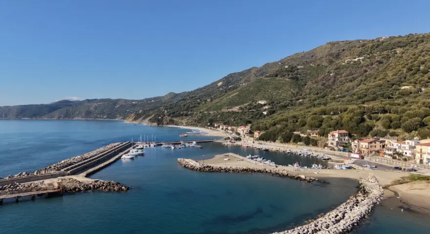 Marina di Pisciotta, con il suo porto turistico e le case aggrappate alla collina verdeggiante, sotto un cielo azzurro.