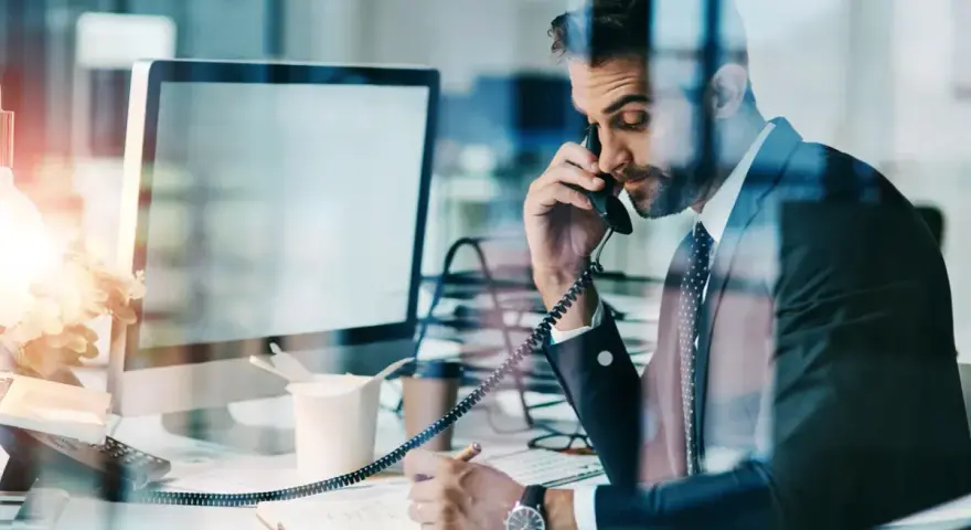Biznesmen w garniturze rozmawia przez telefon, notując w zeszycie. Nawet w obliczu siły wyższej, praca wre.