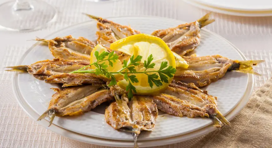 Piatto di alici alla scapece disposte a raggiera, guarnite con fette di limone e prezzemolo.
