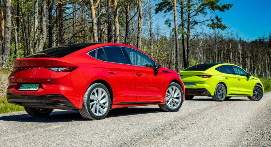 Dwa samochody Skoda Enyaq w kolorach czerwonym i limonkowym na leśnej drodze.