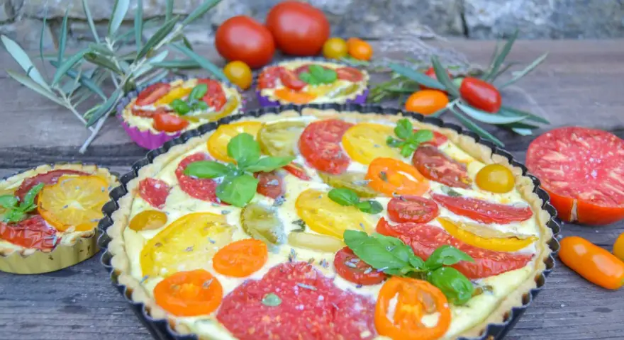 Eine herzhafte Tomaten Quiche mit bunten Tomatenscheiben und frischem Basilikum, garniert mit Lavendelblüten.