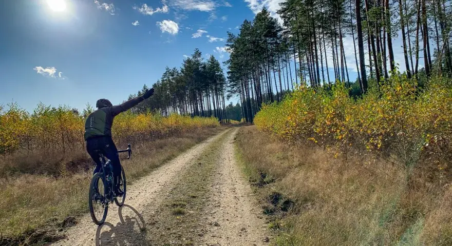 Rowerzysta cieszy się jazdą po szutrowej drodze wśród jesiennych drzew.