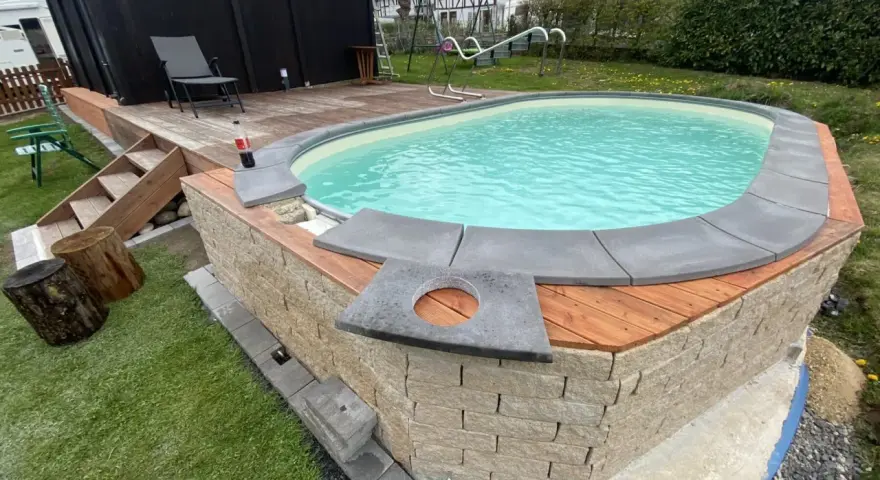 Ein Pool mit selbstgemachten Randsteinen, umgeben von Holz und Naturstein.