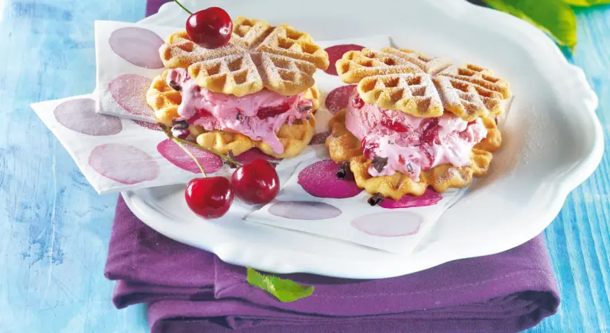 Zwei herzförmige Waffeln gefüllt mit Kirscheis und Schokostückchen, garniert mit frischen Kirschen. Ein süßer Genuss!