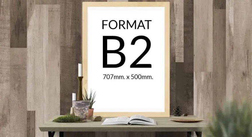 Ramka z napisem "FORMAT B2 707mm. x 500mm." na tle drewnianej ściany. Na stole obok książka i świece.