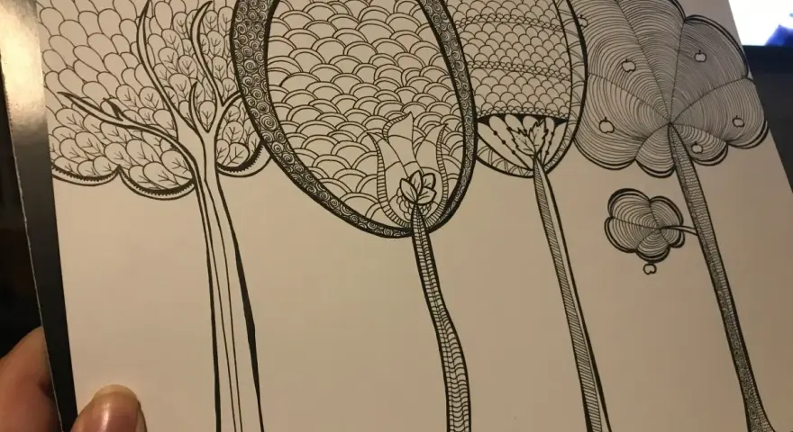 En hand håller ett papper med en detaljerad doodle av fantasifulla träd. Varje träd har unika mönster i kronorna, som om någon ville skapa doodle-konst.