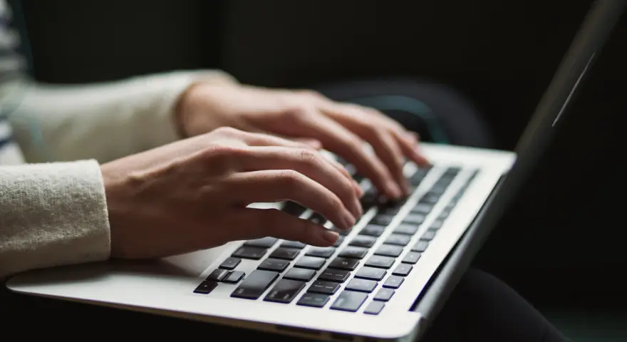 Dłonie piszą na laptopie. Ktoś przygotowuje wypowiedzenie umowy o pracę po angielsku, szukając wzoru.