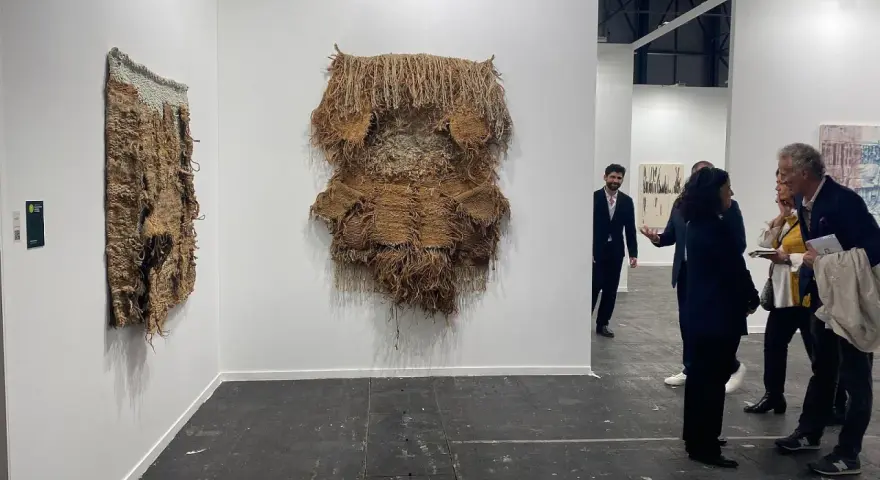 Exposición de arte contemporáneo con tapices texturizados y personas observando.