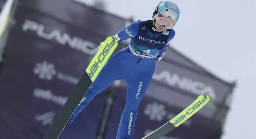 Skoczkini narciarska w locie, w niebieskim kombinezonie, z nartami Fischer. Planica.