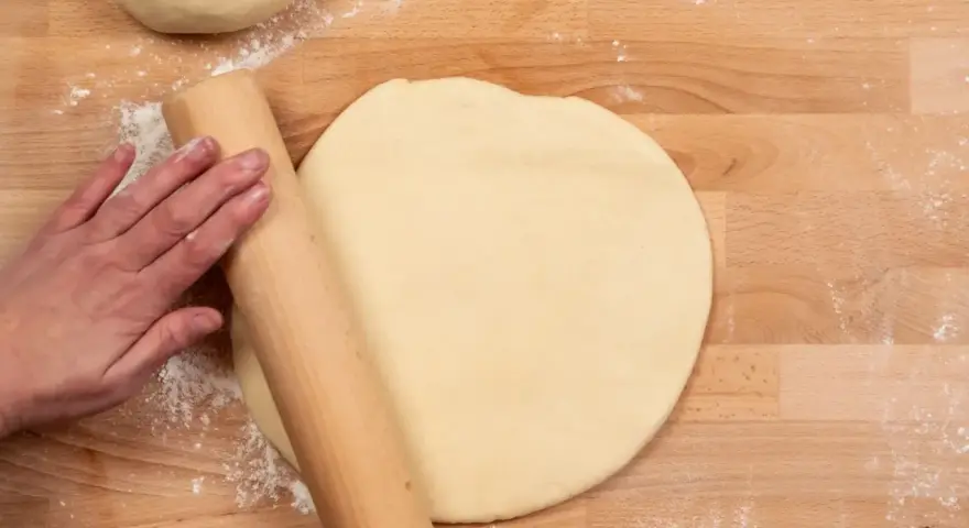 Hand rollt Teig auf Holzbrett aus. Vielleicht mit Dinkelmehl? Was ist Dinkelmehl?