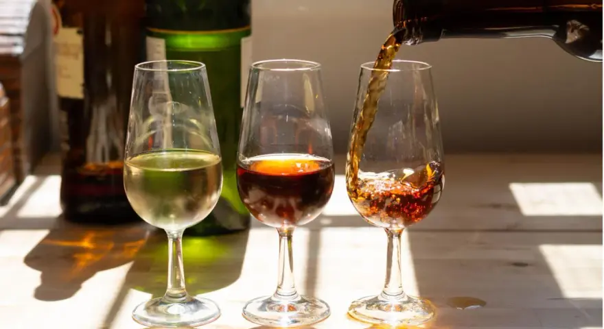 Drei Gläser mit Sherry-Alkohol: ein helles, ein dunkles und ein drittes, in das gerade eingeschenkt wird.