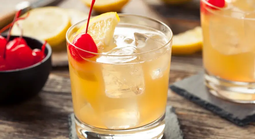 En gyllene whiskey sour med is, citron och körsbär. En klassisk drink som passar perfekt en varm dag.