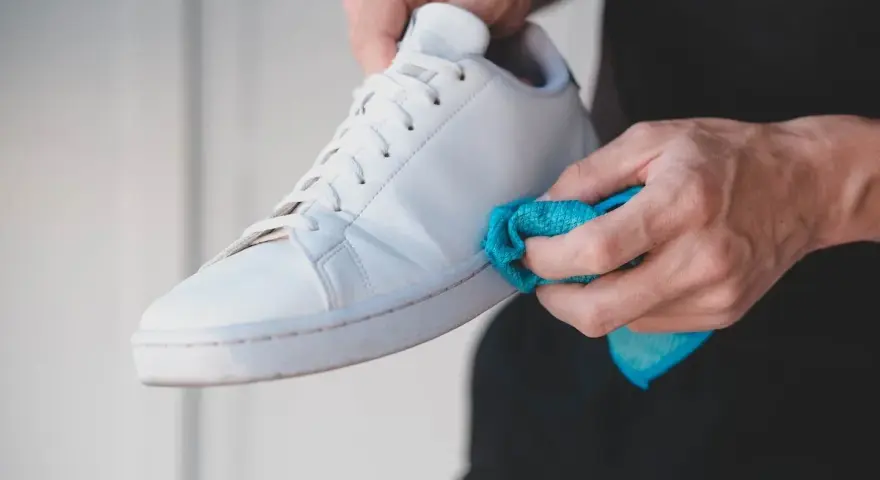 Mani che puliscono una scarpa bianca Adidas Stan Smith con un panno blu. Ecco come lavare le Stan Smith per farle tornare come nuove.