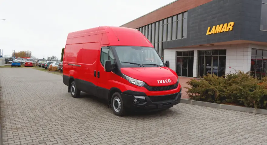 Czerwony bus Iveco na parkingu przed budynkiem z napisem LAMAR.