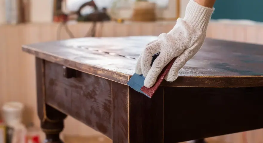 Mano guantata leviga un tavolo antico, un'idea per trasformare mobili antichi in moderni con un tocco di fai-da-te.